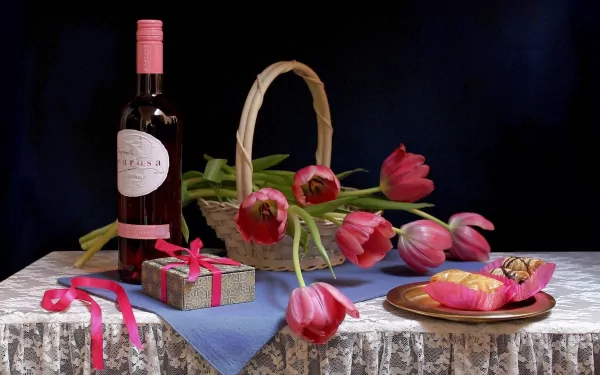 Still life featuring a bottle of wine, a basket of tulips, a gift box with a ribbon, and colorful sweets on a lace tablecloth, creating a vibrant and inviting atmosphere.