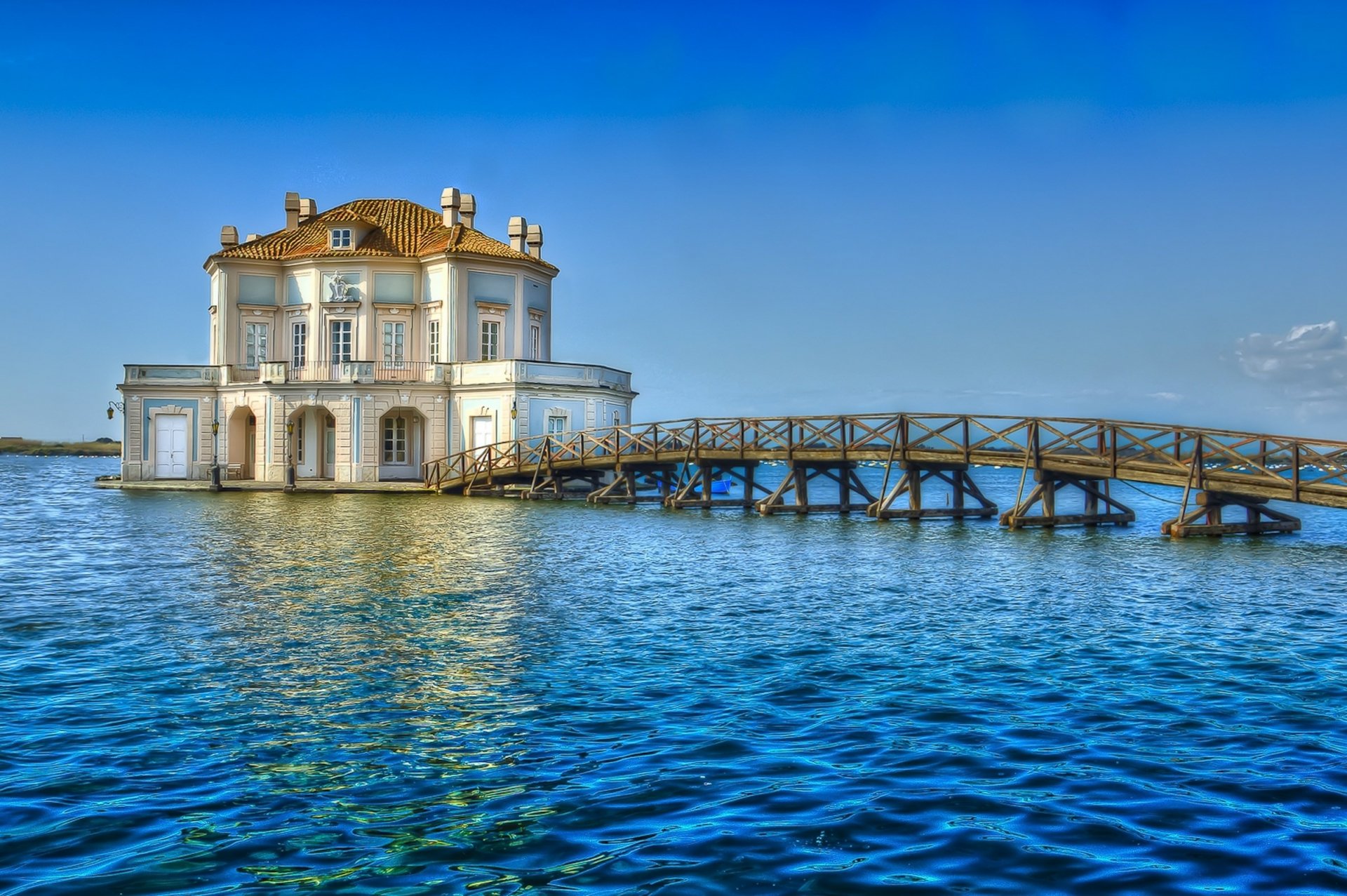 A stunning view of Casina Vanvitelliana, a man-made structure, surrounded by serene blue waters and a wooden walkway, captured in high-definition for a desktop wallpaper.