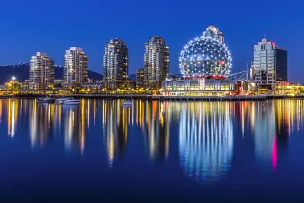 A stunning night view of Vancouver's skyline, featuring vibrant city buildings and a prominent illuminated dome reflecting on the water, creating a captivating man-made landscape.