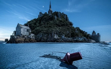 A captivating HD desktop wallpaper featuring a serene beach scene with a buoy in the foreground and an ancient building perched atop a rocky hill, illuminated under a twilight sky.