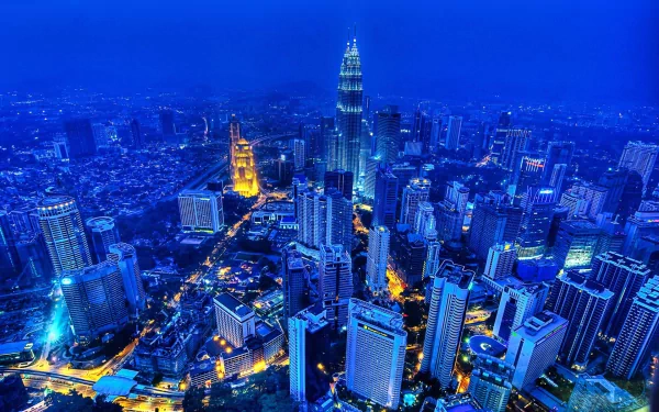 A stunning HD view of Kuala Lumpur at night, showcasing the iconic Petronas Towers amidst a vibrant cityscape filled with modern architecture and twinkling lights.