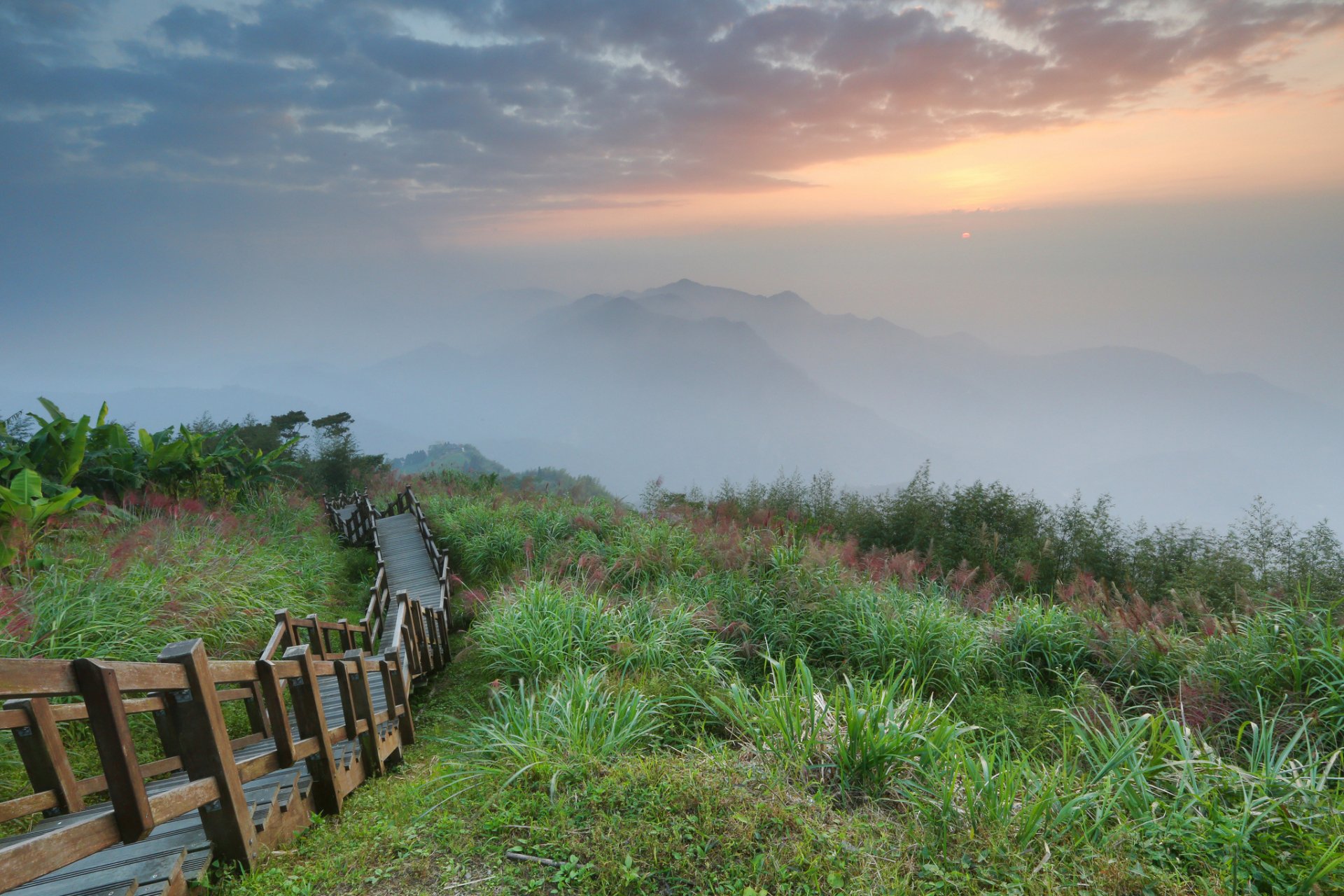 HD desktop wallpaper showing man-made wooden stairs winding through lush greenery with misty mountains and a colorful sky in the background.