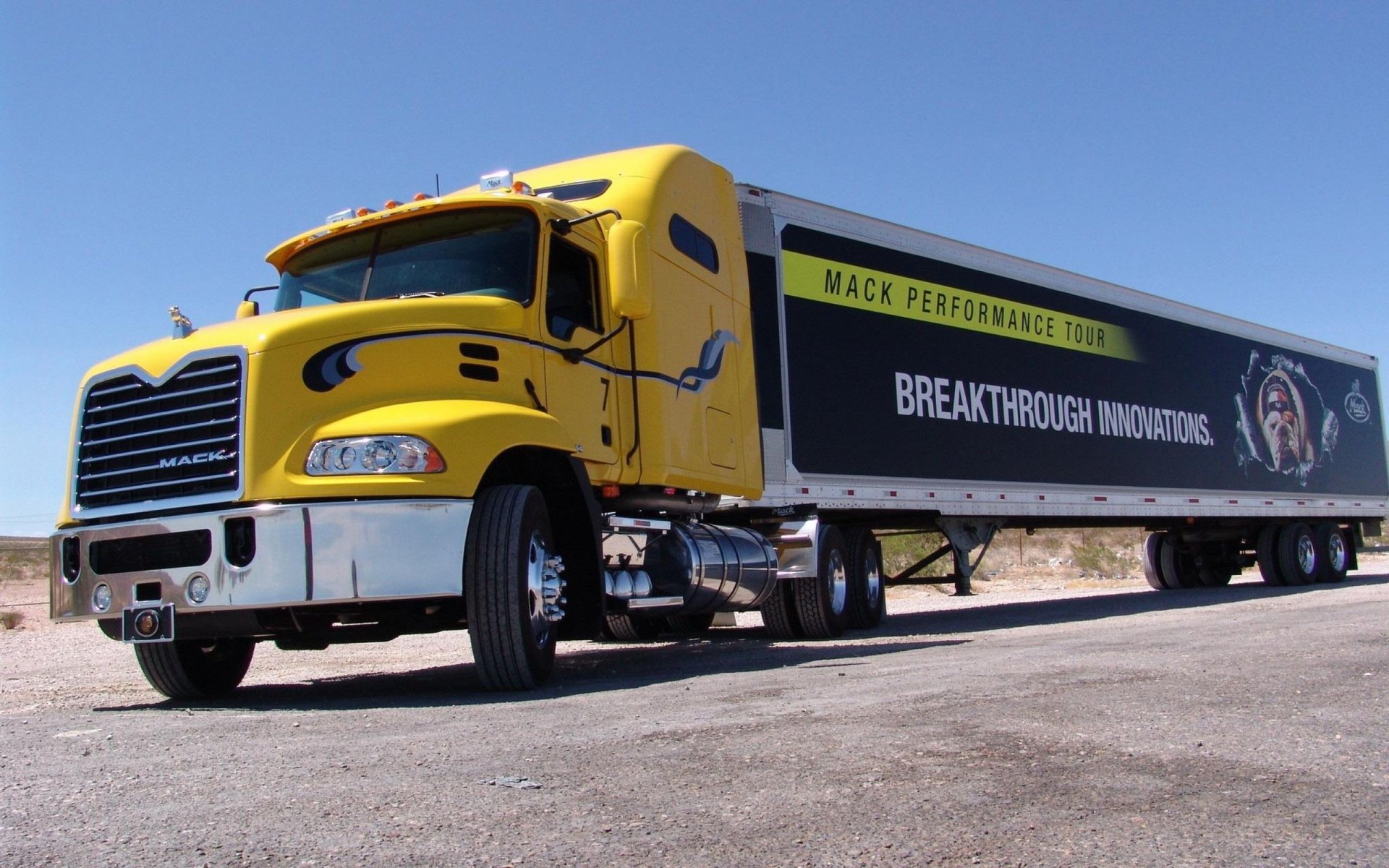HD desktop wallpaper featuring a yellow Mack Trucks vehicle with a trailer displaying Breakthrough Innovation in a clear, sunny outdoor setting.