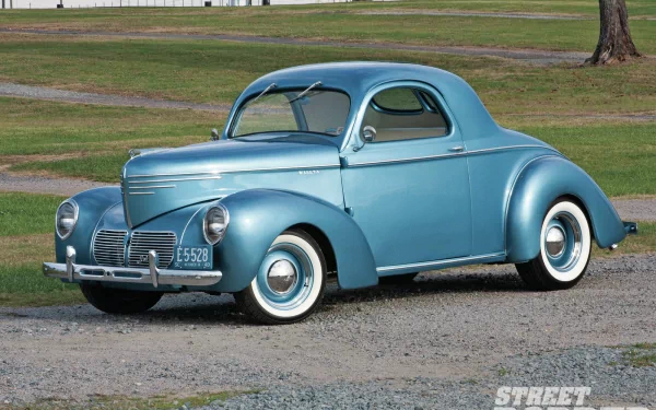 HD PC desktop wallpaper: light-blue 1940 Chevrolet coupe parked on gravel in a grassy park, showcasing chrome trim and whitewall tires.
