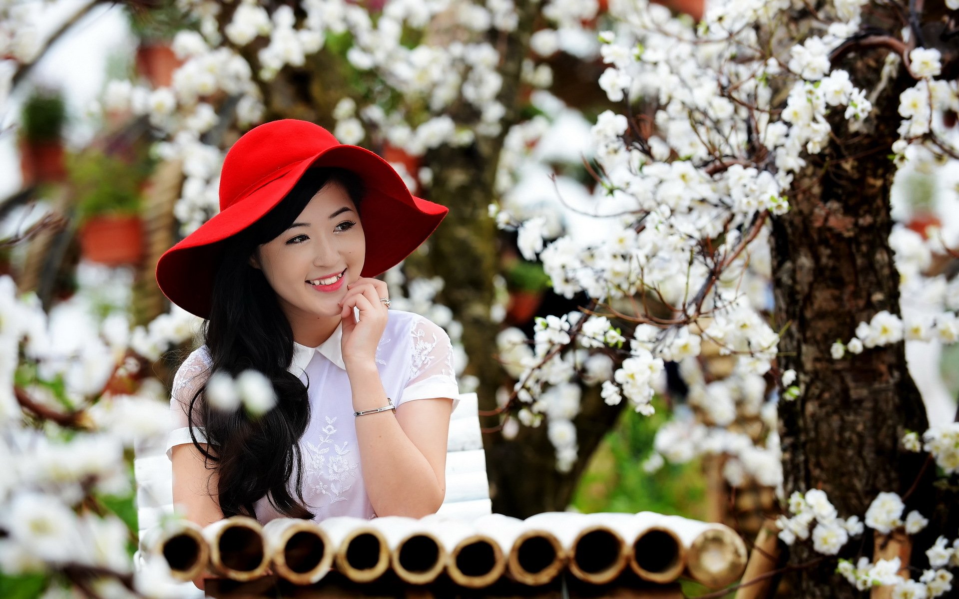 HD PC desktop wallpaper showing an Asian woman in a red hat smiling among blooming white flowers on tree branches.