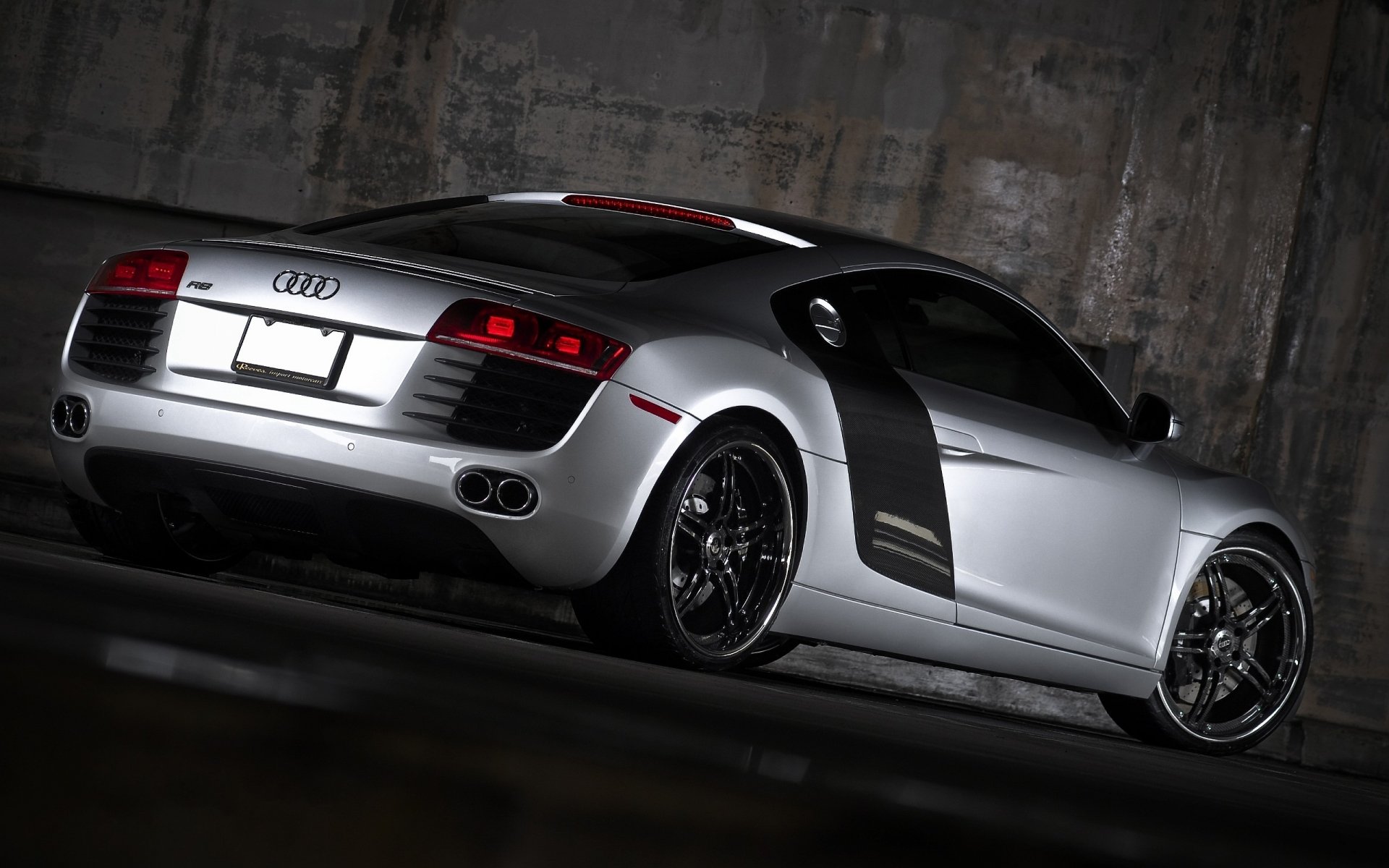 A sleek Audi R8 parked in a dimly lit space, showcasing its distinctive rear design and modern curves, serves as a captivating HD PC desktop wallpaper and background.