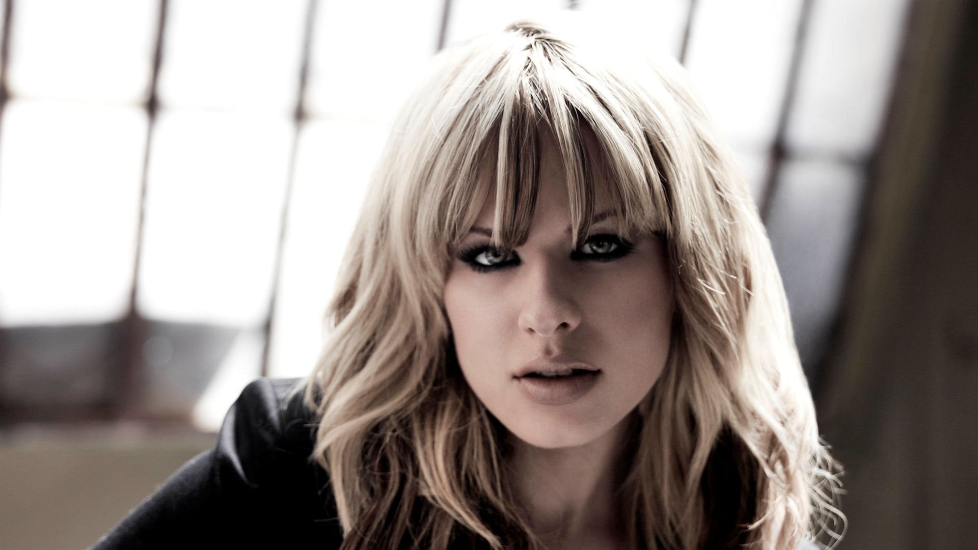 HD PC desktop wallpaper featuring a close-up portrait of Orianthi with blonde hair and intense gaze, set against a softly lit background.