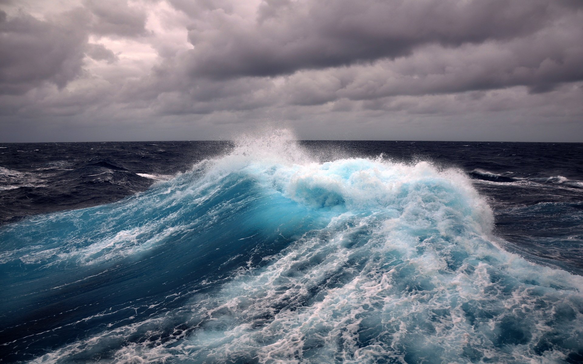 A dramatic ocean wave crashes against a dark, cloudy sky, capturing the power and beauty of nature in this HD desktop wallpaper.
