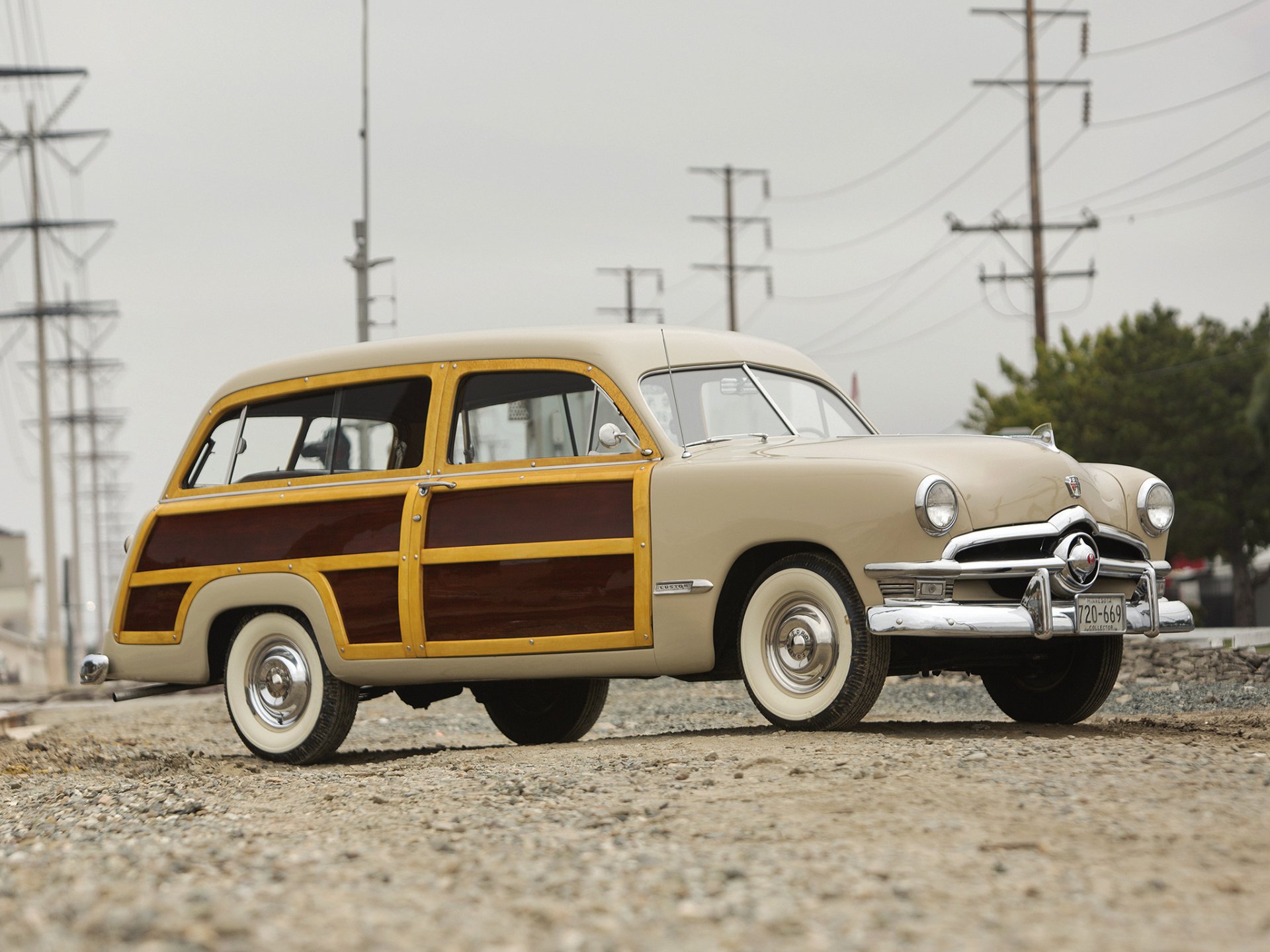 HD desktop wallpaper featuring a classic 1950 Ford Custom Squire station wagon with wood paneling, parked on a gravel road under an overcast sky.