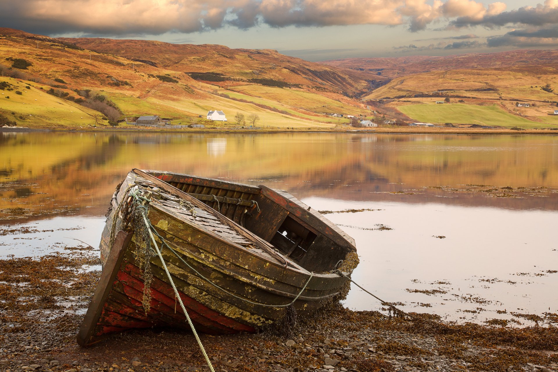 HD desktop wallpaper showing an old wooden boat resting on a calm shore with rolling hills and cloudy sky in the background.