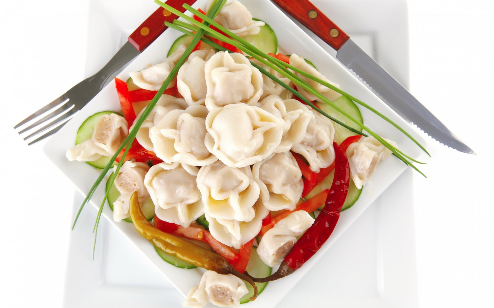 A vibrant plate of dumplings is beautifully arranged with colorful peppers and cucumber slices, showcased as a high-definition PC desktop wallpaper and background.