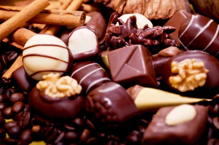 HD desktop wallpaper of assorted chocolates, featuring various shapes and toppings, including nuts and stripes, against a background of cinnamon sticks and coffee beans. Tags: food, chocolate.