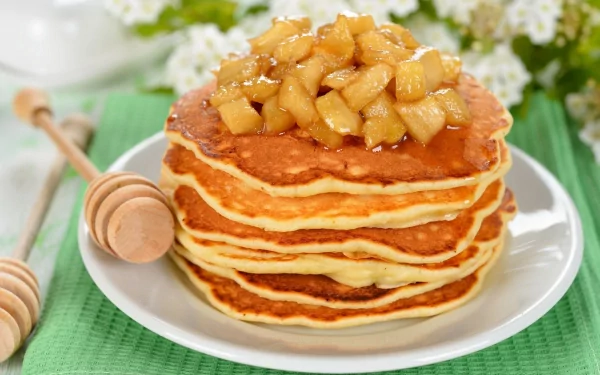 HD desktop wallpaper featuring a stack of fluffy pancakes topped with cooked apples, accompanied by a honey dipper, set on a green placemat.