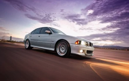 HD desktop wallpaper featuring a silver BMW E39 driving on an open road under a dramatic purple and blue sky.