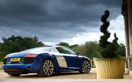 A stunning blue Audi R8 supercar parked near a decorative plant, set against a dramatic cloudy sky, showcased as a high-definition PC desktop wallpaper.