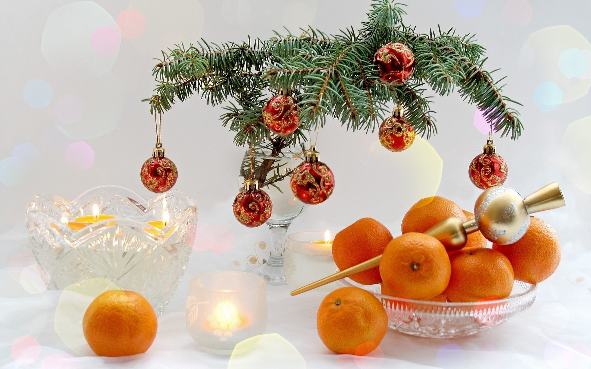 A festive scene featuring a decorated evergreen branch with Christmas ornaments, glowing candles, and a bowl of oranges, capturing the warmth of the holiday season.