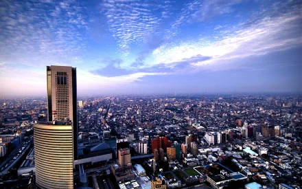 2K Quad HD PC desktop background showing man-made Tokyo skyline at dusk—high-rises and sprawling urban grid beneath a dramatic cloud-streaked sky.