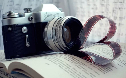 A classic camera rests on an open book, with a strip of film creatively draped nearby, capturing the essence of photography and literature in this HD desktop wallpaper.