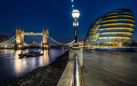 A stunning HD wallpaper featuring London’s iconic Tower Bridge illuminated at night, alongside the modern architecture of City Hall, reflecting on the River Thames.