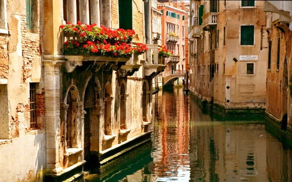 HD wallpaper of a serene Venice canal in Italy, showcasing historic man-made architecture with vibrant flowers and reflections on the water.