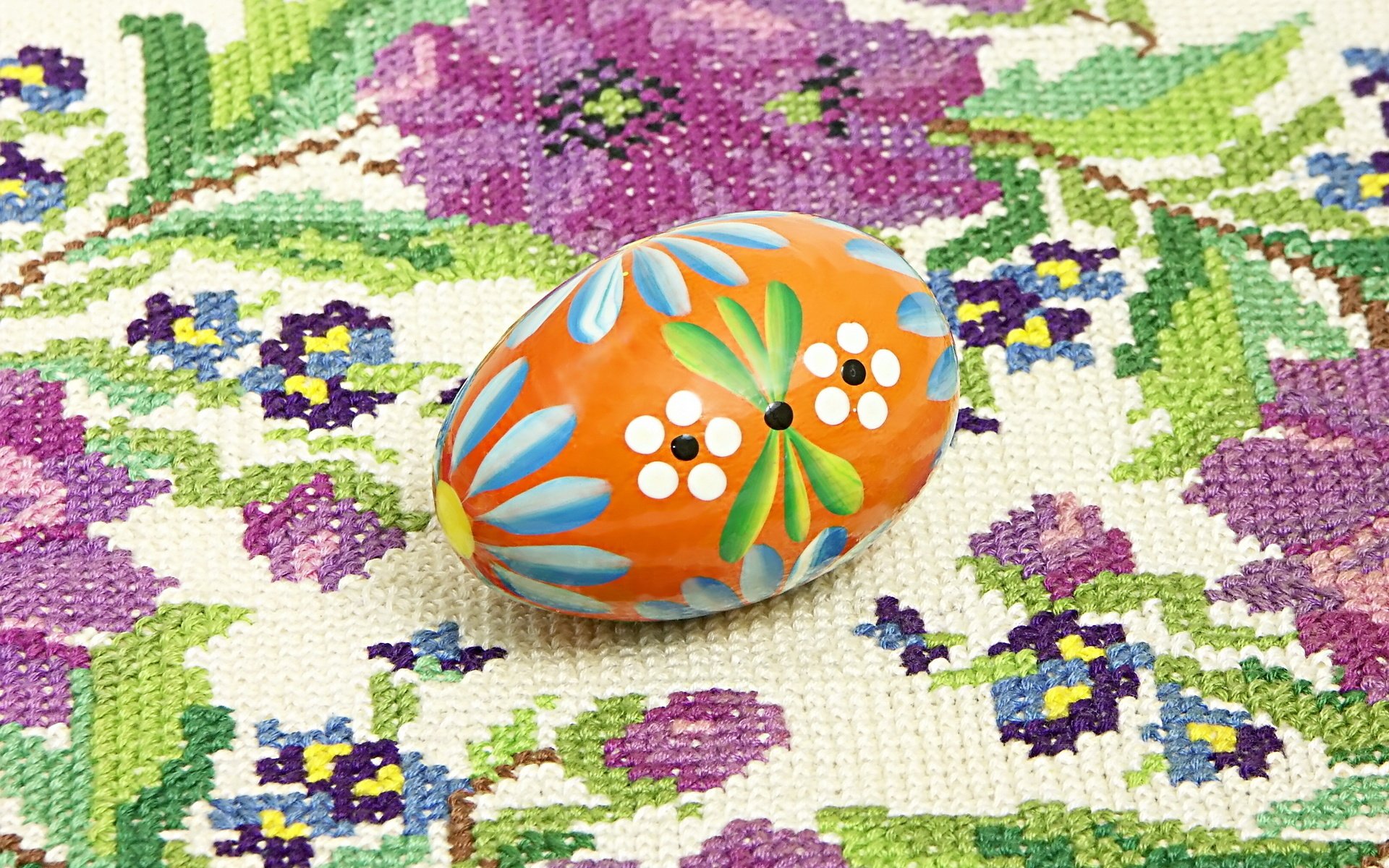 A vibrant Easter egg with floral designs rests on a colorful textile background, creating a festive and cheerful holiday atmosphere in this HD desktop wallpaper.