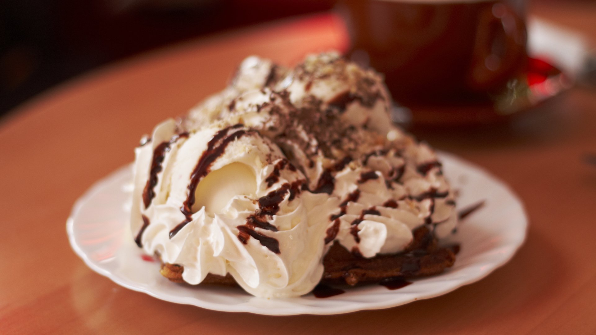 A tempting dessert topped with whipped cream and chocolate drizzle sits on a white plate, complemented by a warm cup of coffee, creating a mouthwatering food scene in a 4K Ultra HD wallpaper.