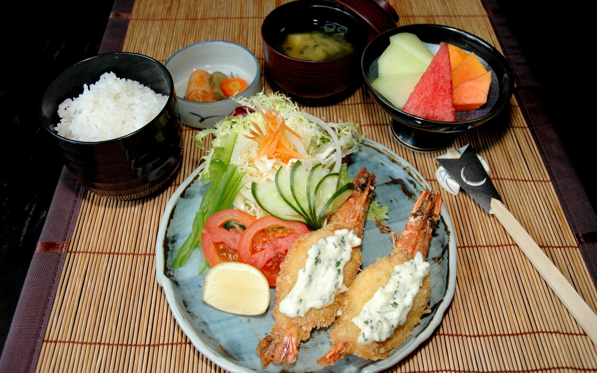 HD PC desktop wallpaper featuring a meal with fried shrimp topped with sauce, fresh salad, rice, miso soup, pickles, and fruit on a bamboo mat background.