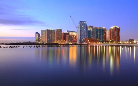 HD desktop wallpaper showcasing the illuminated Jersey City skyline at dusk, reflecting on calm waters under a clear blue sky.