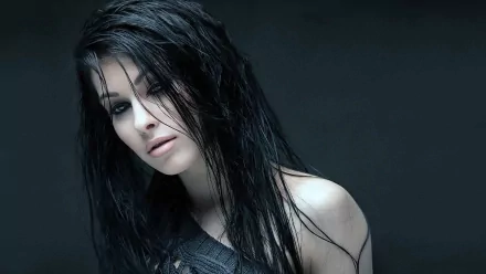 A striking HD wallpaper featuring a beautiful woman with long, dark hair, gazing thoughtfully into the distance against a dark background.