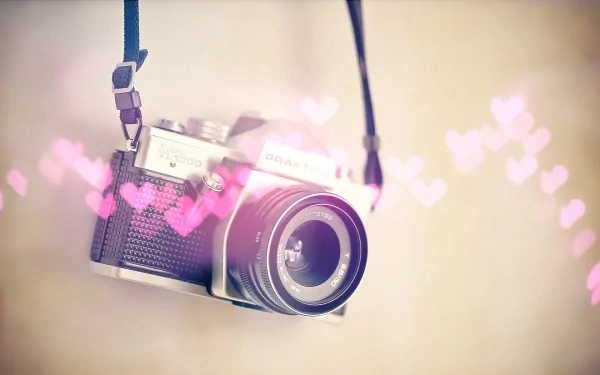 A stylish camera hangs against a soft background adorned with pink hearts, creating a charming and whimsical HD desktop wallpaper.