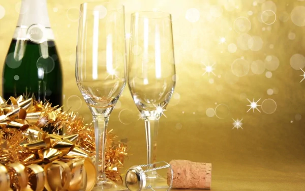 HD desktop wallpaper featuring two empty champagne glasses, a bottle, cork, and gold holiday decorations against a sparkling golden background for New Year celebration.