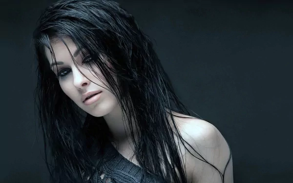 A striking HD wallpaper featuring a beautiful woman with long, dark hair, gazing thoughtfully into the distance against a dark background.