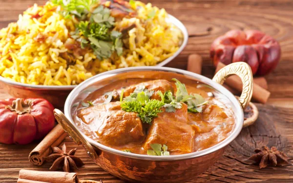 A vibrant HD desktop wallpaper featuring a delicious meal of aromatic rice and curry, garnished with fresh herbs, surrounded by spices on a rustic wooden background.