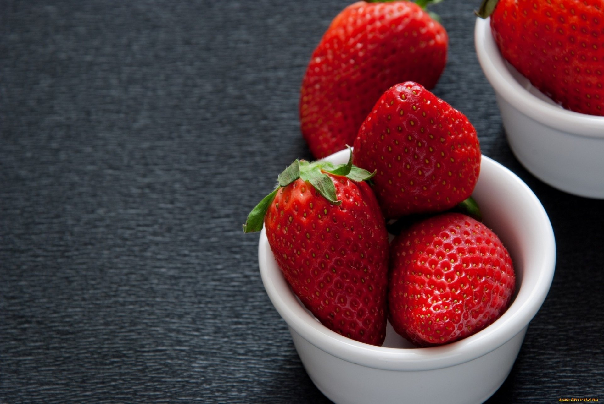 HD PC desktop wallpaper featuring fresh, vibrant strawberries in white bowls on a dark textured surface, highlighting the rich red color and natural texture of the fruit.