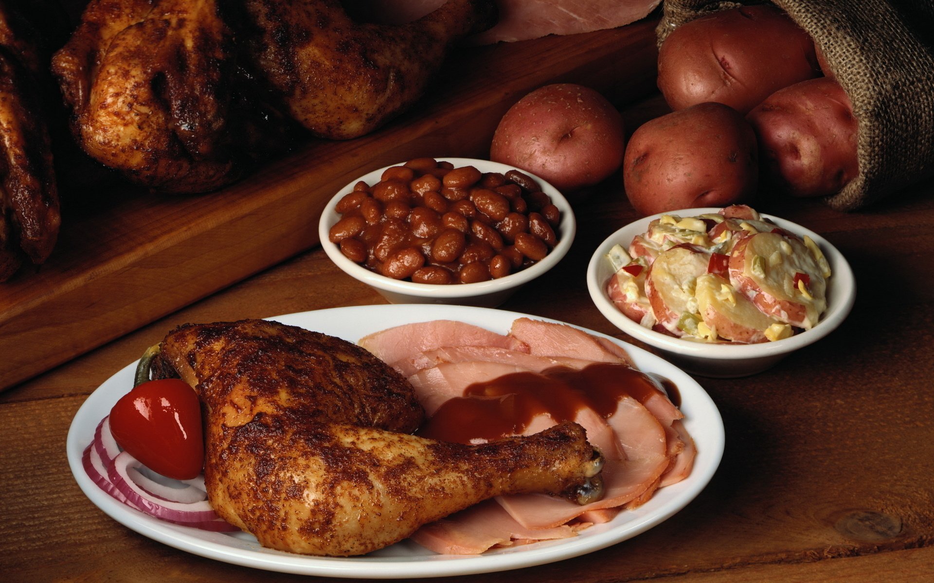A delicious meal featuring seasoned roasted chicken, sliced ham, baked beans, creamy coleslaw, and fresh potatoes, captured in high-definition for an enticing desktop wallpaper.