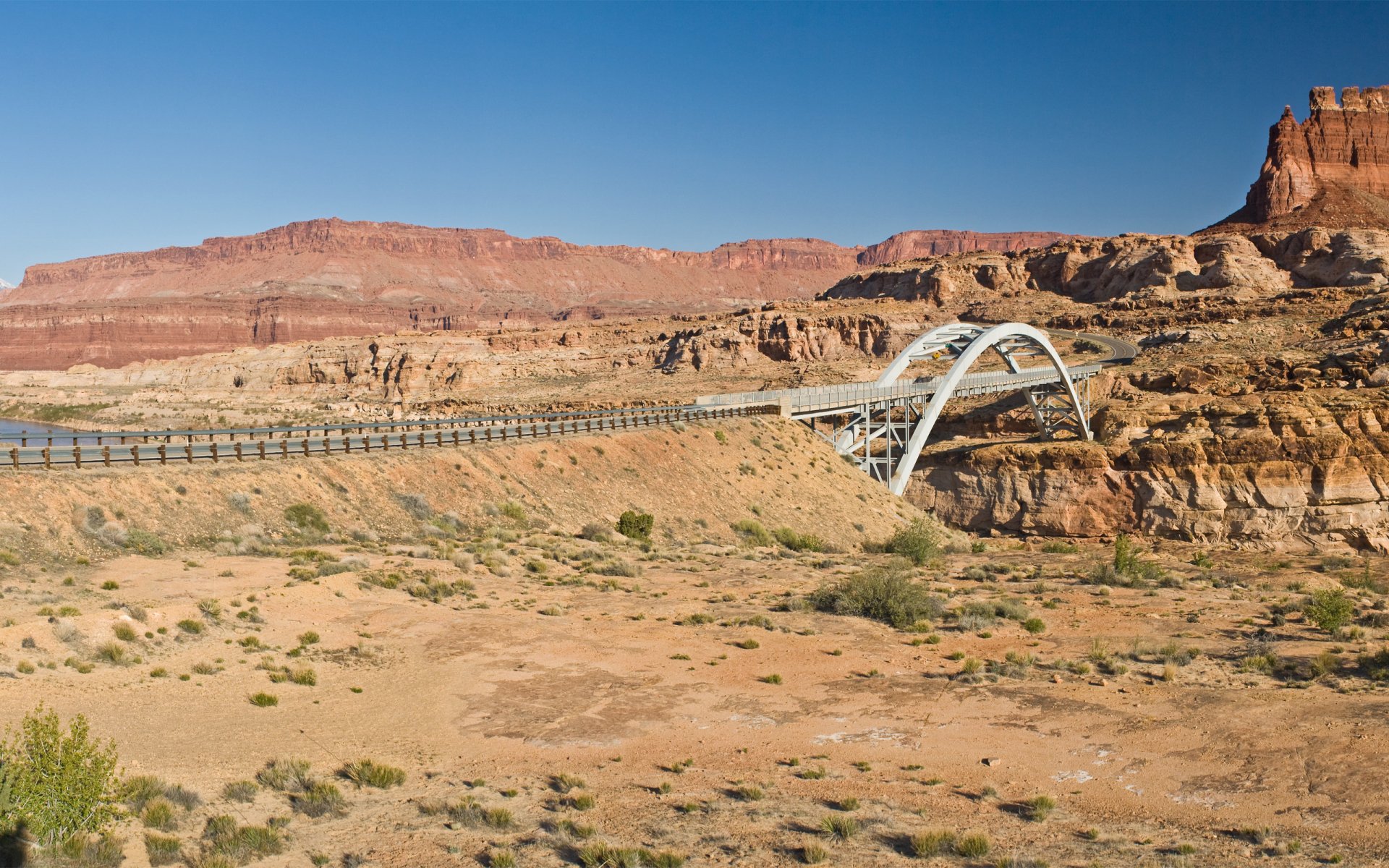 HD desktop wallpaper showing a man-made bridge spanning a desert landscape with rocky formations under a clear blue sky.