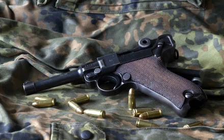 HD PC desktop wallpaper featuring a man-made Luger pistol resting on camouflage fabric with scattered brass bullet casings.