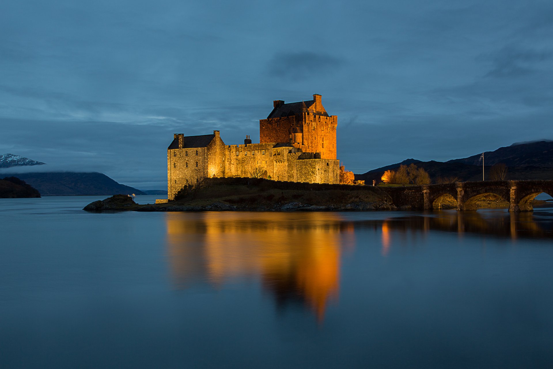 A stunning HD wallpaper of a illuminated castle by the water at dusk, showcasing man-made architecture against a serene landscape. The warm lights reflect beautifully in the calm waters.