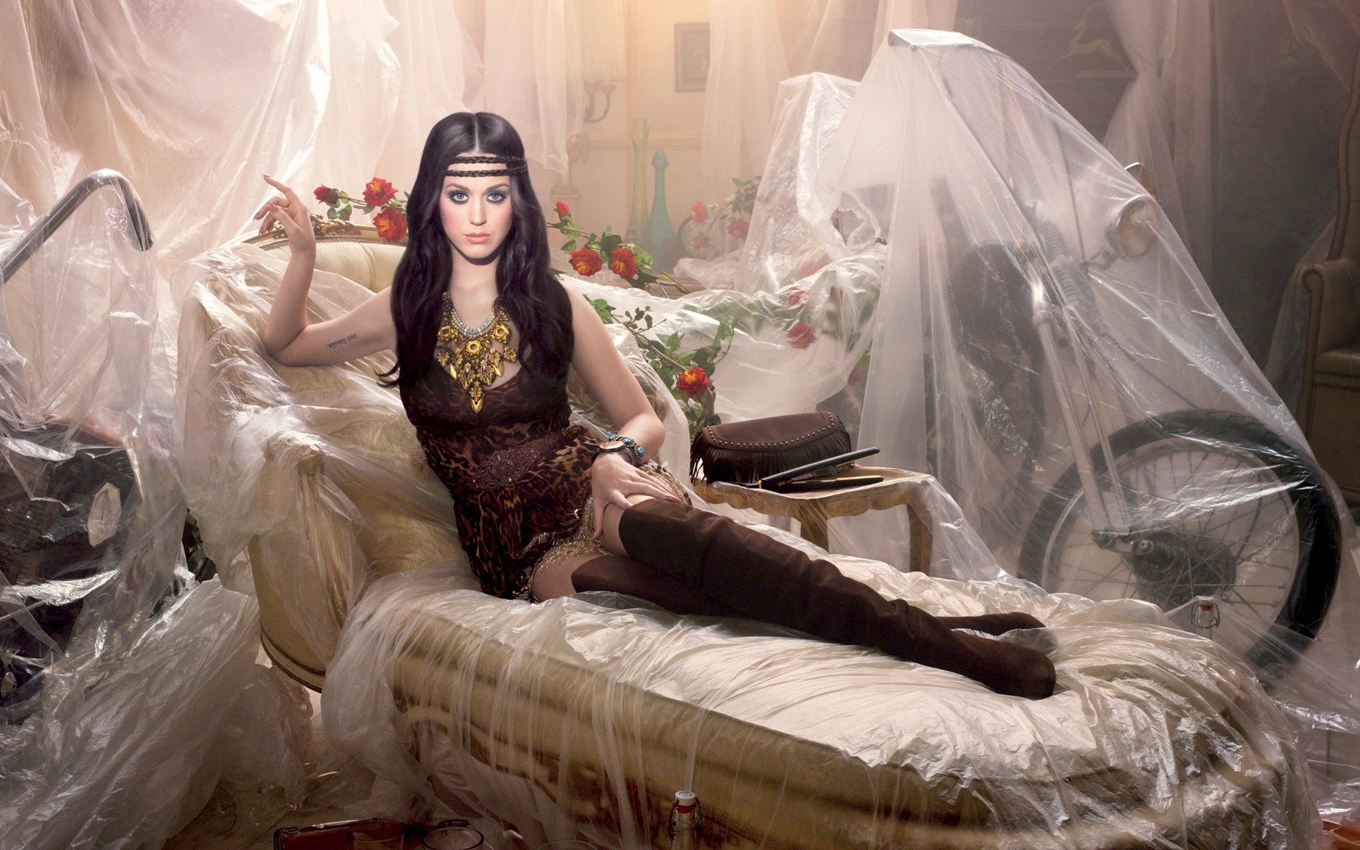 HD desktop wallpaper featuring Katy Perry in an artistic setting, sitting on a vintage couch surrounded by draped plastic sheets.