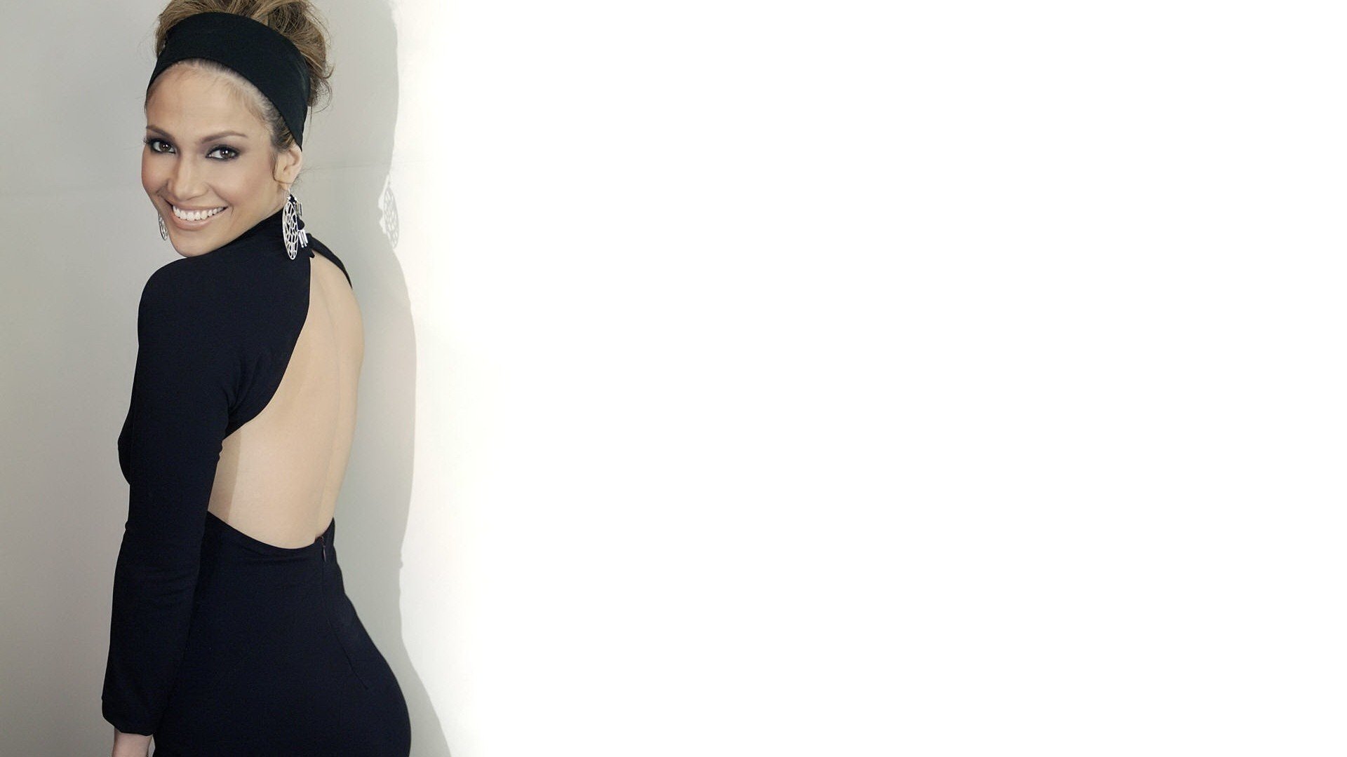 HD PC desktop wallpaper featuring a smiling Jennifer Lopez in a stylish black backless dress against a plain white background.