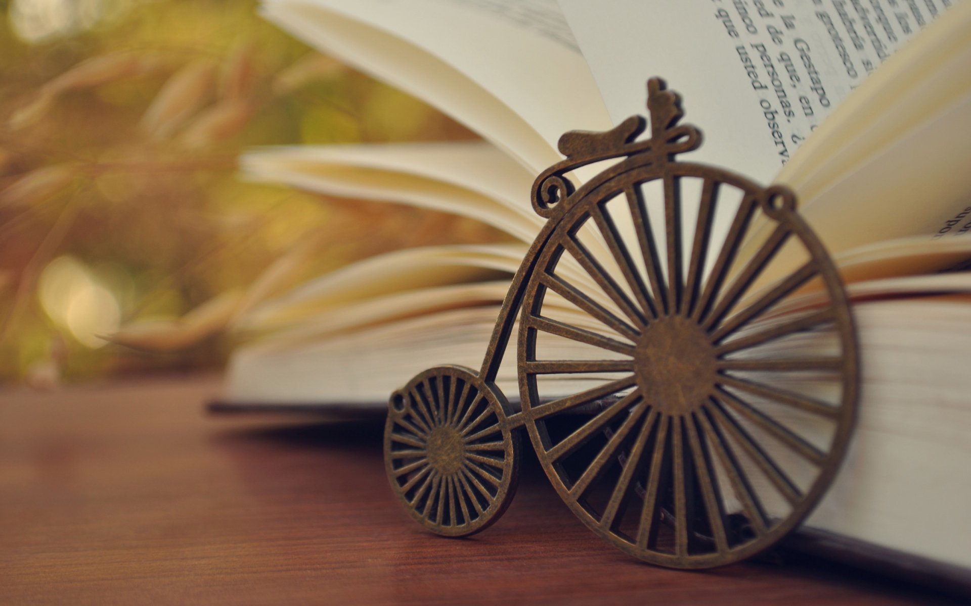 A close-up HD desktop wallpaper featuring a small man-made vintage bicycle sculpture in front of an open book with blurred text and a warm background.