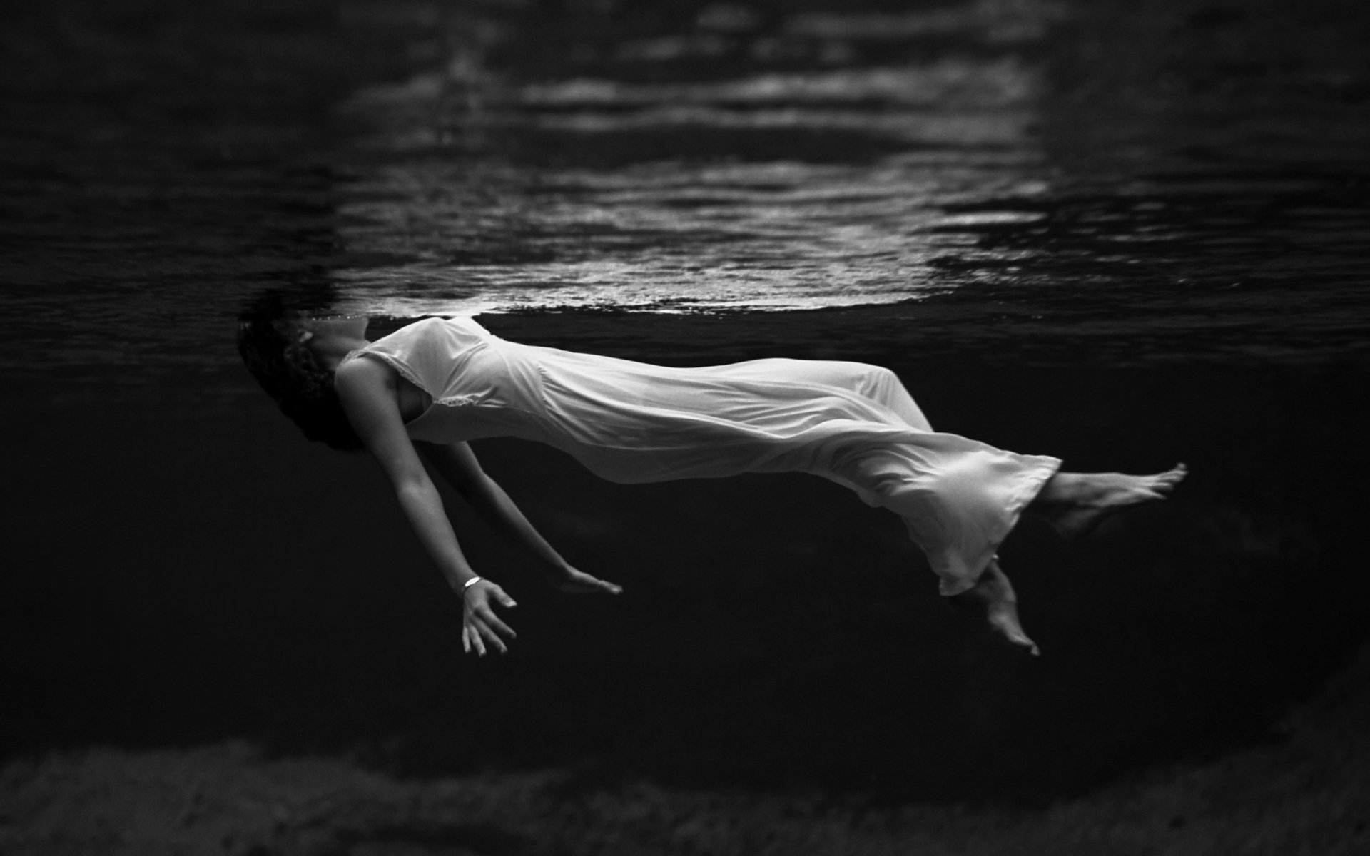 A serene black and white HD desktop wallpaper of a woman in a flowing dress floating underwater, capturing a calm and introspective mood.