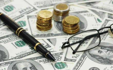 A close-up of currency notes, coins, a pen, and glasses, creating a rich, man-made backdrop that highlights the theme of money for an HD desktop wallpaper.