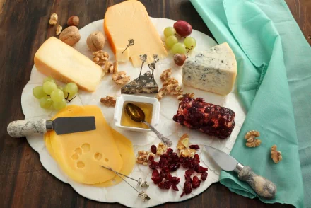 HD desktop wallpaper featuring an assortment of cheeses, grapes, walnuts, dried cranberries, and a honey dipper on a white platter with a turquoise cloth nearby.
