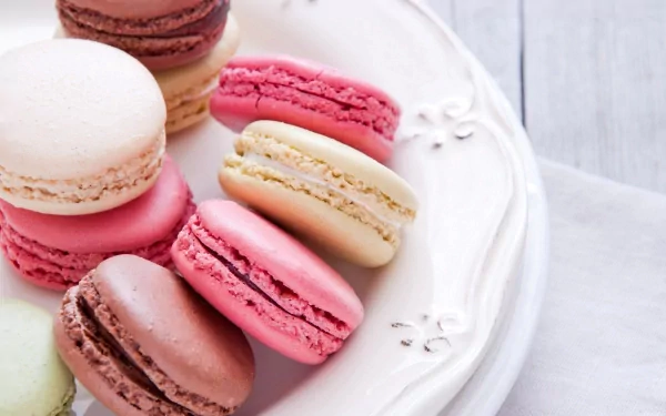 A colorful assortment of macarons displayed on a decorative plate, featuring shades of pink, cream, and brown, creates a delightful food-themed HD desktop wallpaper.
