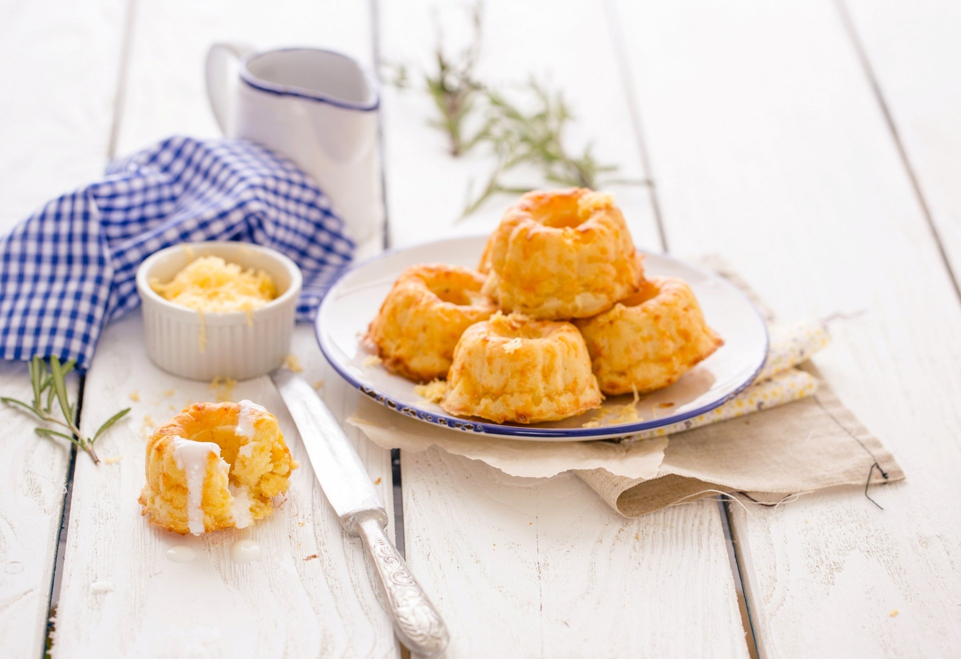 A delightful display of sweet cupcakes on a white plate, accompanied by a small bowl of frosting and a blue checkered napkin, creating a tempting dessert scene.