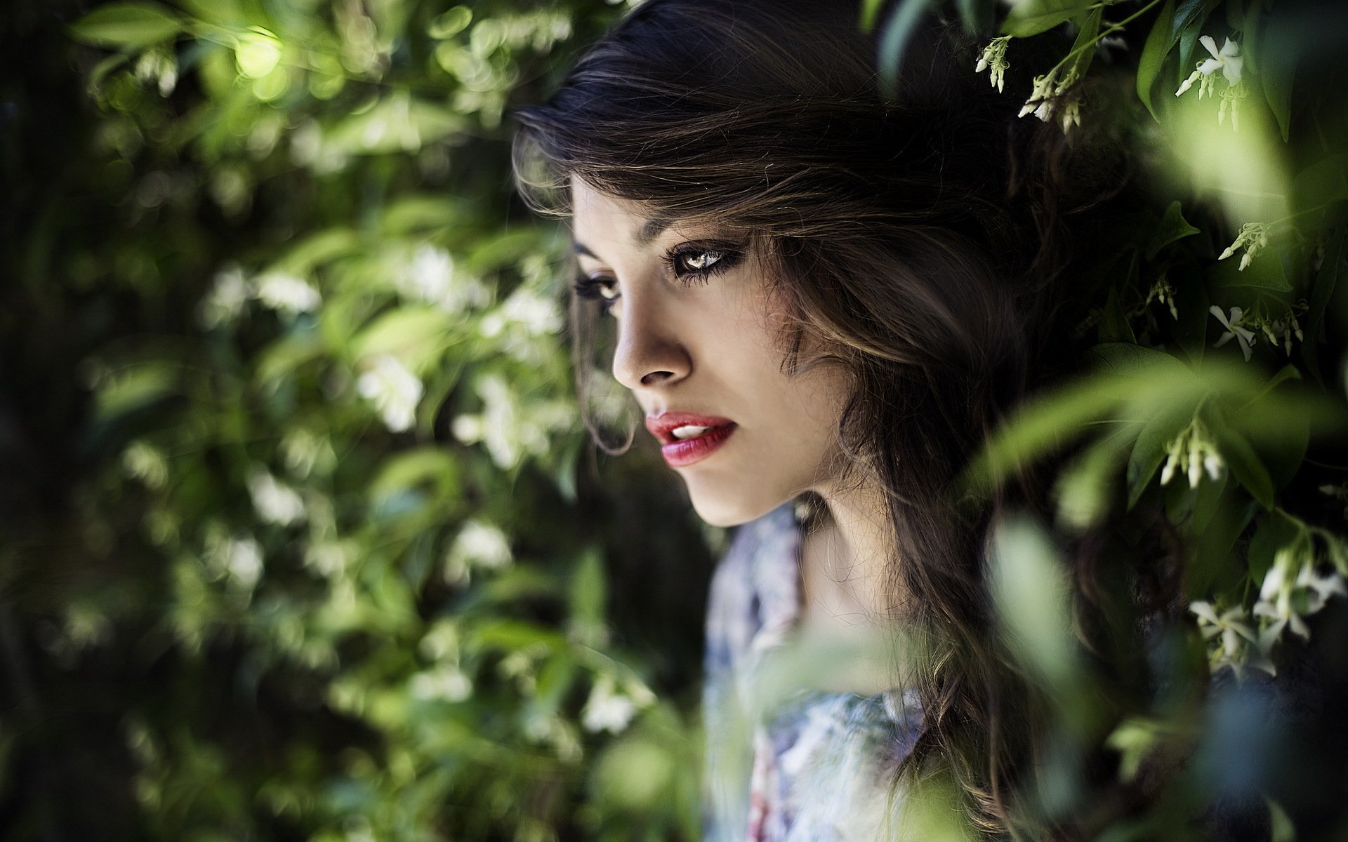 A close-up of a woman’s face framed by lush greenery, showcasing her features and expression. This HD image serves as a striking desktop wallpaper or background.