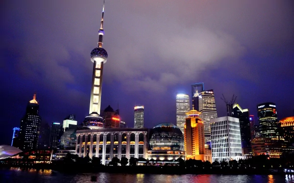 HD desktop wallpaper of Shanghai's illuminated skyline at night, featuring iconic man-made skyscrapers and the Oriental Pearl Tower under a cloudy sky.
