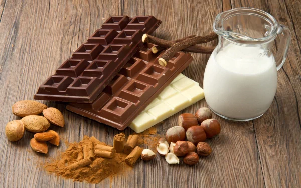 An elegant HD desktop wallpaper featuring an assortment of chocolate bars, nuts, and a jug of milk on a wooden surface, highlighting a rich and inviting food theme.