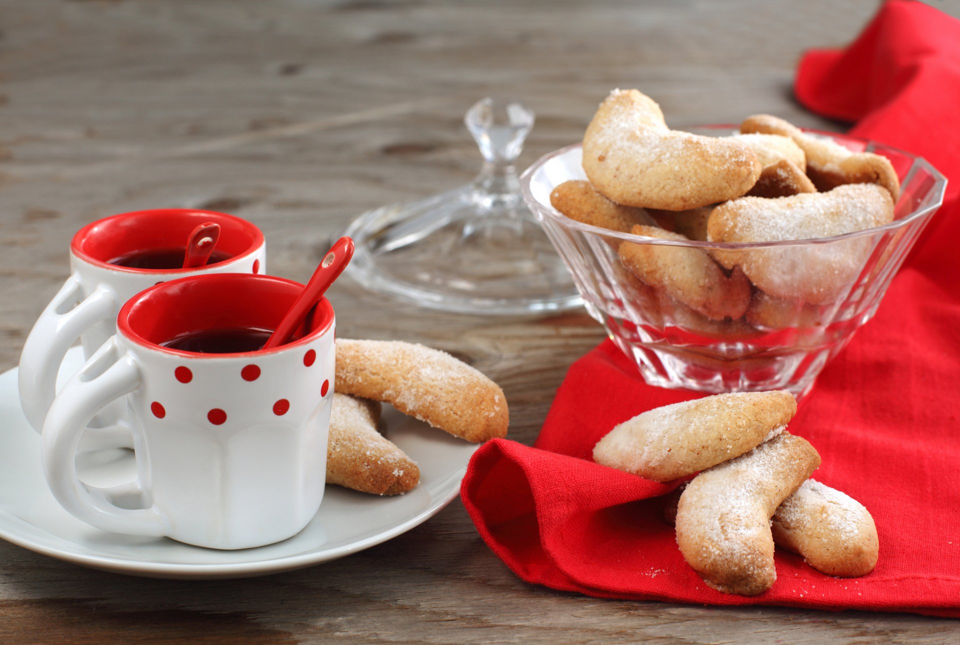 HD PC desktop wallpaper featuring a wooden table with two cups of red beverage and crescent-shaped cookies on a plate and in a glass bowl, accented by a red cloth.
